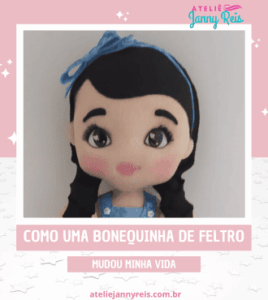 Bonequinha de feltro com laço azul, olhos expressivos e roupas delicadas, criada artesanalmente por Ateliê Janny Reis.